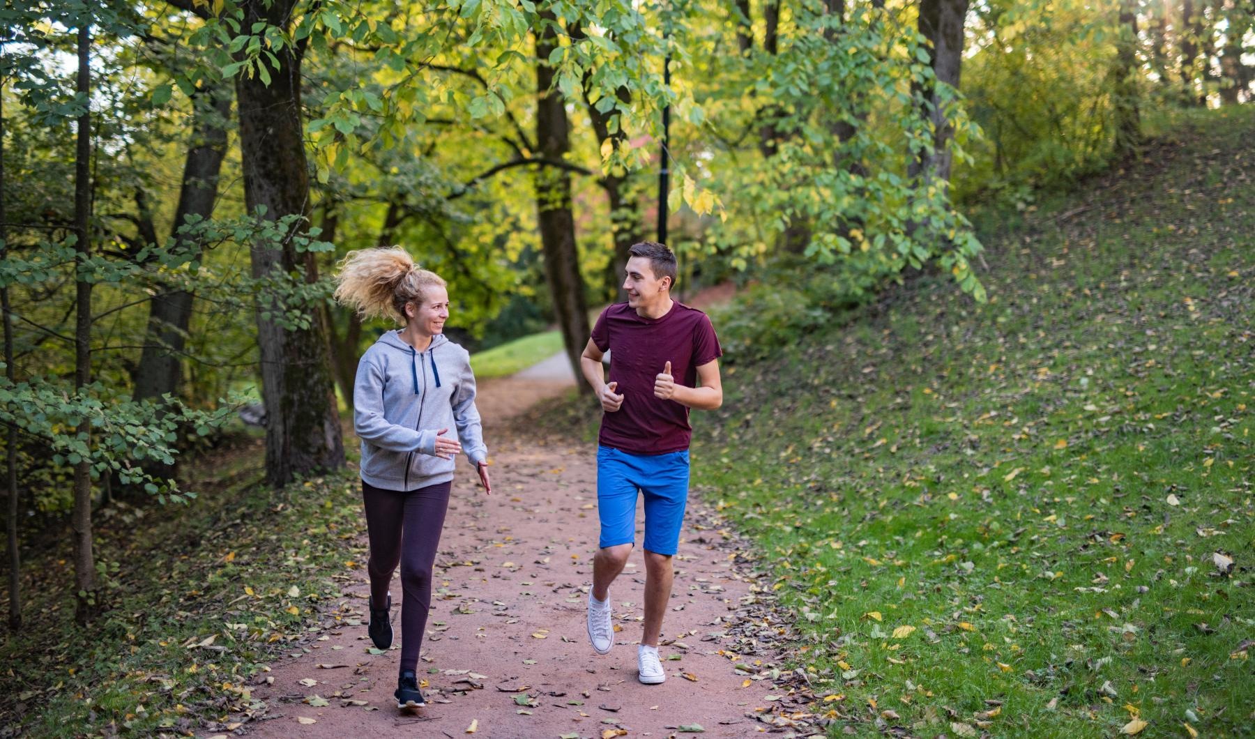 The essence of exceptional living A man and woman running on a path in a forest at Heritage Grove apartments in Broken Arrow, OK